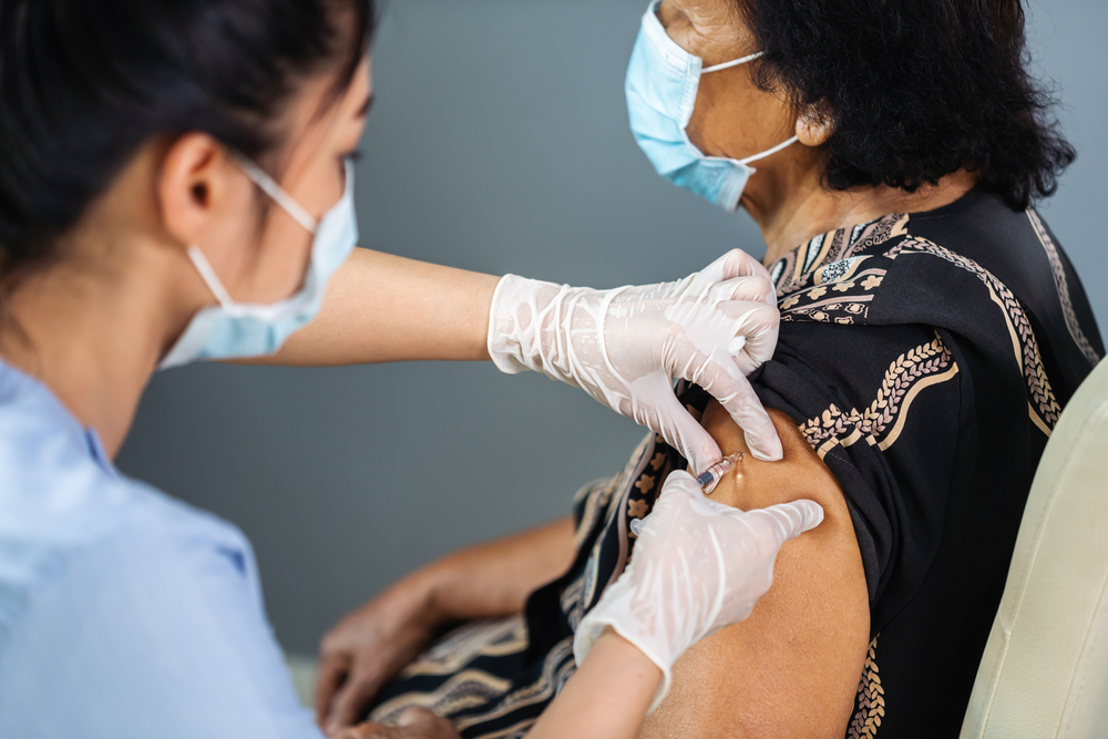 Doctor in gloves and mask injects masked senior patient with vaccine.